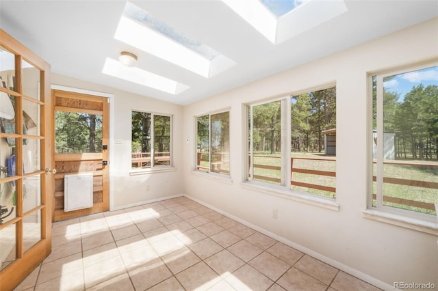 unfurnished sunroom with a skylight, plenty of natural light, tile patterned flooring, and baseboards