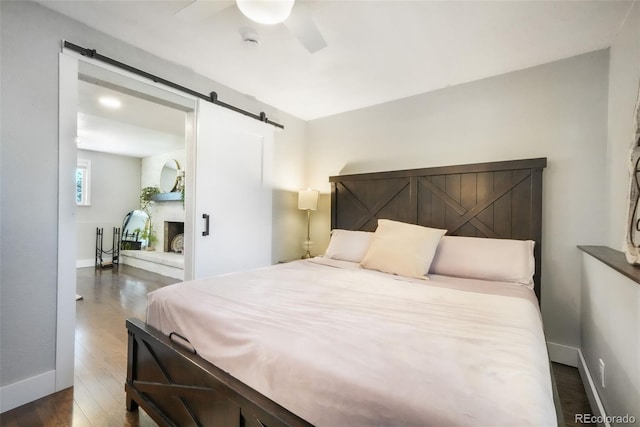 bedroom featuring a barn door, wood finished floors, baseboards, and ceiling fan