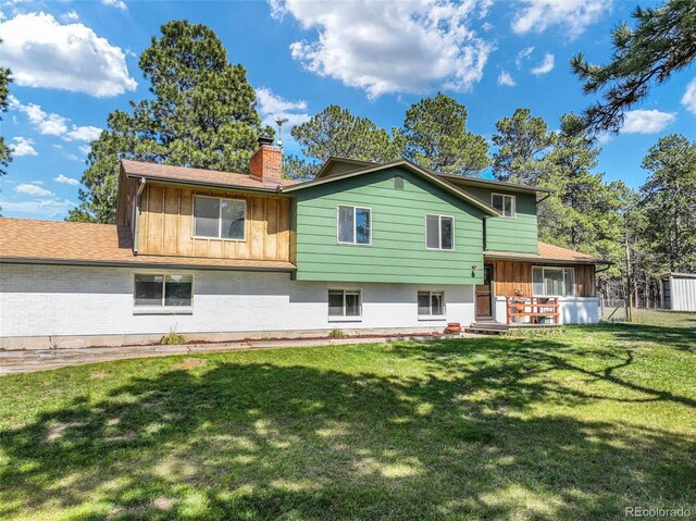 back of house featuring a chimney, a lawn, board and batten siding, and brick siding