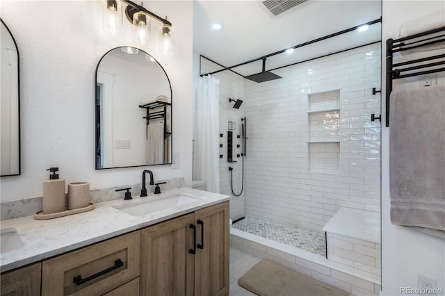 full bathroom featuring a tile shower and double vanity