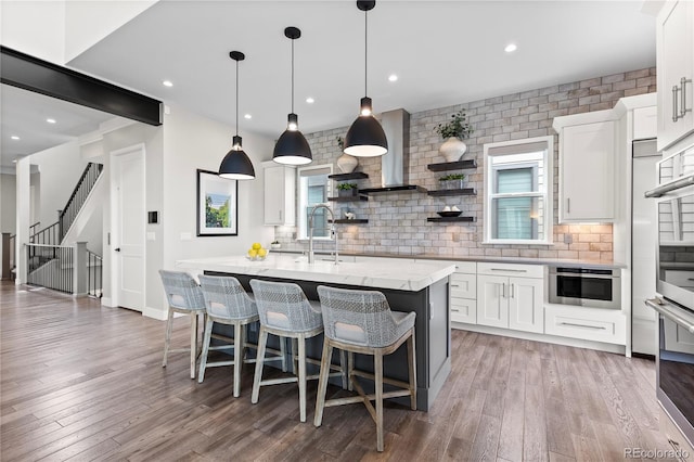 10113 Bellwether Ln, Lone Tree, CO 80124 - kitchen featuring a center island with sink, wall chimney exhaust hood, white cabinetry, a sink, and backsplash