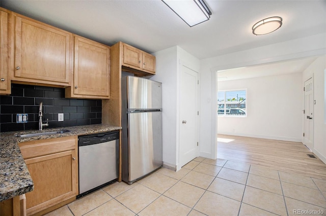 kitchen with appliances with stainless steel finishes, a sink, light tile patterned floors, decorative backsplash, and baseboards
