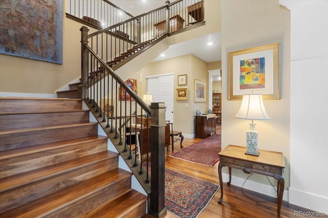 stairway with a high ceiling, baseboards, and wood finished floors