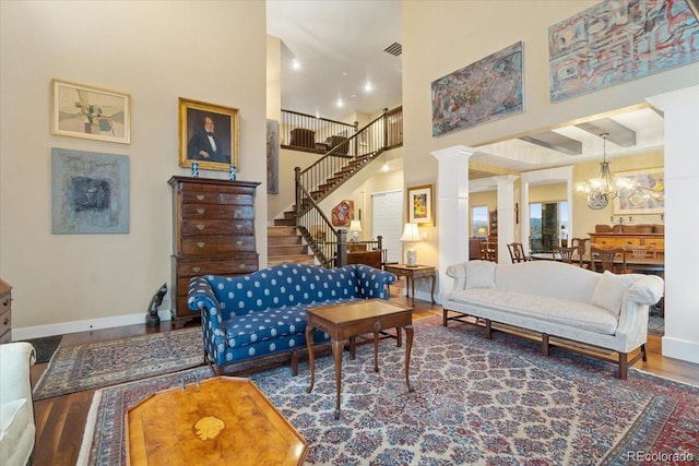 living room with baseboards, an inviting chandelier, stairs, a towering ceiling, and ornate columns