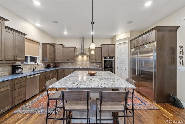 kitchen with wall chimney range hood, stainless steel appliances, a sink, and a breakfast bar