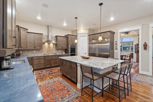 kitchen featuring a center island, dark wood-style flooring, wall chimney range hood, tasteful backsplash, and appliances with stainless steel finishes