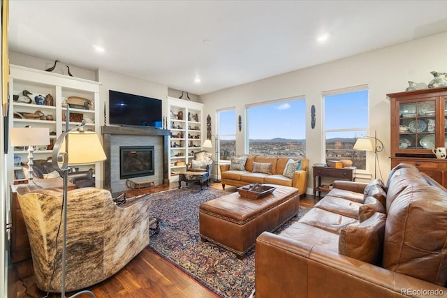 living room with built in shelves, a glass covered fireplace, and dark wood finished floors