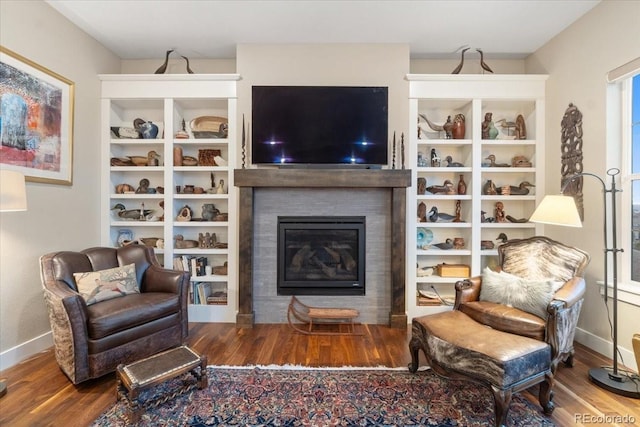 living area with baseboards, a glass covered fireplace, and wood finished floors