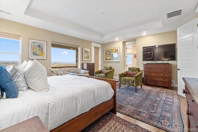 bedroom with multiple windows, a raised ceiling, visible vents, and wood finished floors