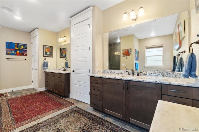 full bath with baseboards, tiled shower, two vanities, and a sink