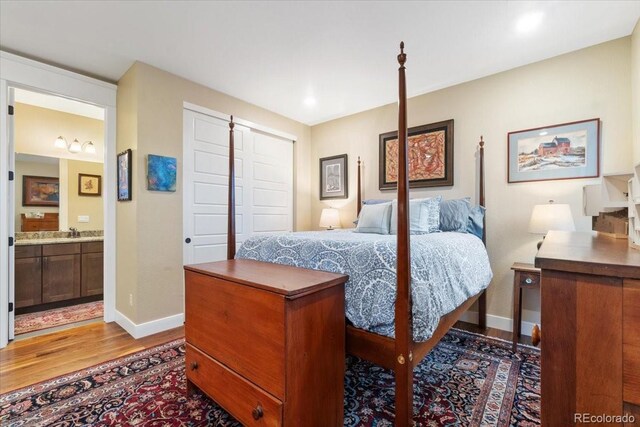 bedroom with a closet, baseboards, a sink, connected bathroom, and wood finished floors