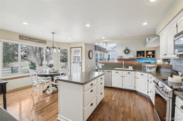 kitchen with dark countertops, wood finished floors, appliances with stainless steel finishes, and a peninsula
