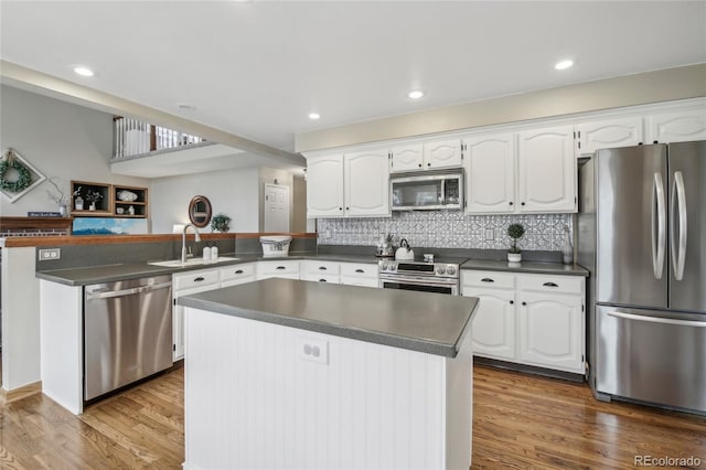 kitchen with white cabinetry, stainless steel appliances, a sink, dark countertops, and a peninsula