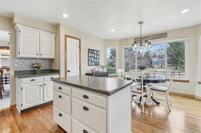 kitchen with a center island, light wood-style flooring, dark countertops, white cabinets, and decorative backsplash