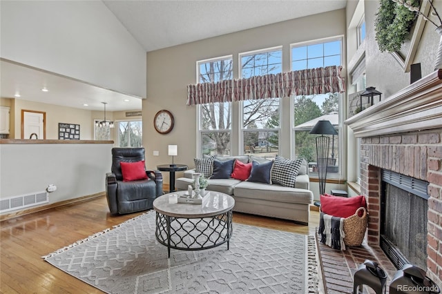 living room featuring high vaulted ceiling, a wealth of natural light, visible vents, a fireplace, and wood finished floors