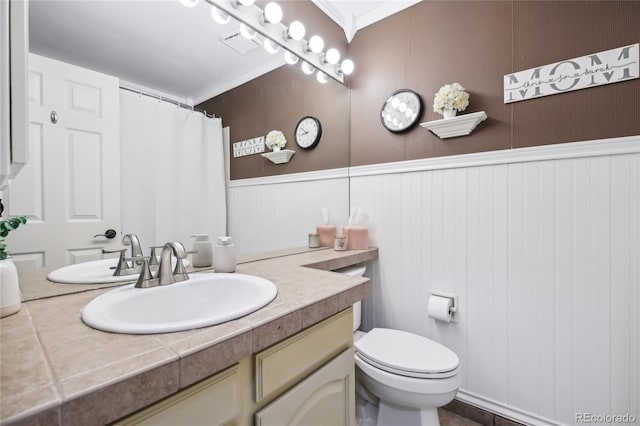 bathroom with vanity, toilet, ornamental molding, visible vents, and wainscoting