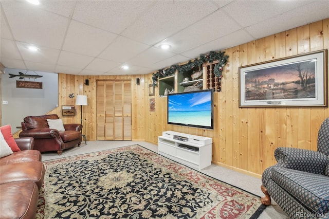 living room featuring wooden walls, carpet flooring, and a drop ceiling