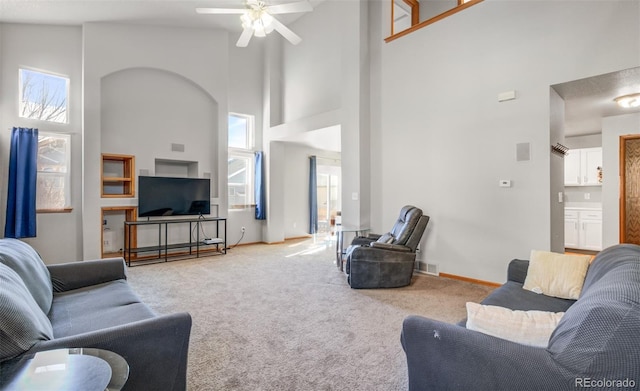 living area featuring light colored carpet, visible vents, a high ceiling, a ceiling fan, and baseboards