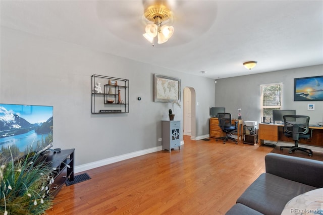 home office with light wood finished floors, baseboards, arched walkways, and ceiling fan