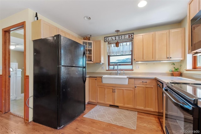 kitchen featuring light countertops, a sink, black appliances, and light brown cabinetry