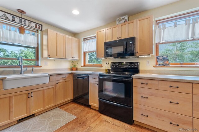 kitchen featuring black appliances, light countertops, a sink, and light brown cabinetry