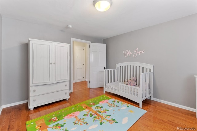 unfurnished bedroom featuring a crib, baseboards, and wood finished floors