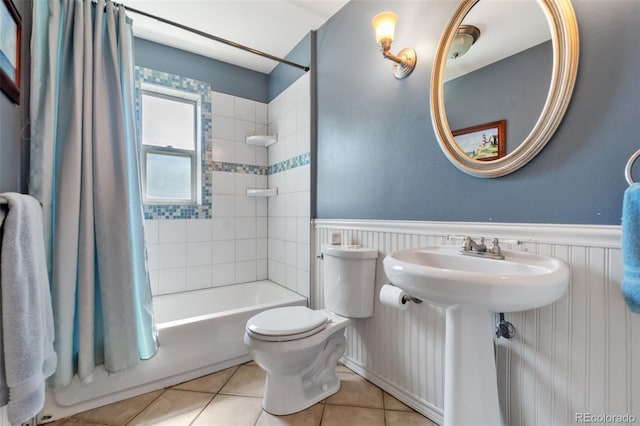 full bath featuring toilet, tile patterned floors, shower / bath combination with curtain, and wainscoting