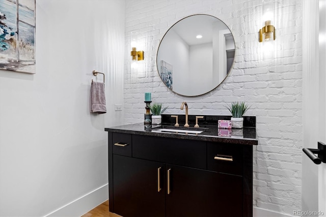 bathroom with baseboards, wood finished floors, vanity, and brick wall