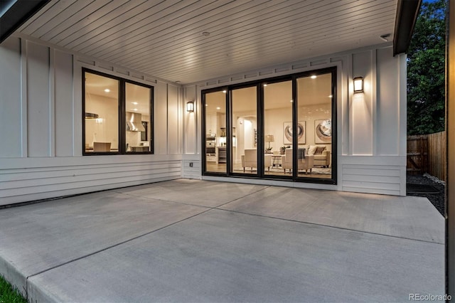 view of exterior entry with board and batten siding, fence, and a patio area