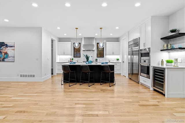 kitchen featuring visible vents, wall chimney range hood, wine cooler, stainless steel appliances, and a breakfast bar area