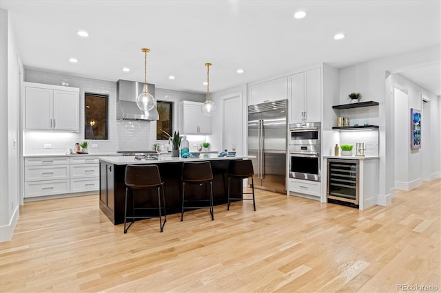 kitchen with wall chimney exhaust hood, light countertops, appliances with stainless steel finishes, wine cooler, and backsplash