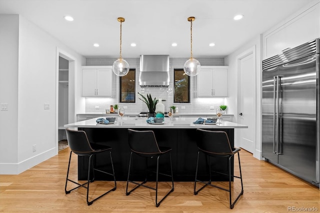 kitchen with tasteful backsplash, a center island, wall chimney range hood, white cabinetry, and stainless steel built in refrigerator