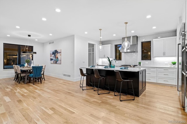 kitchen with light countertops, light wood-style floors, wall chimney range hood, and a kitchen island