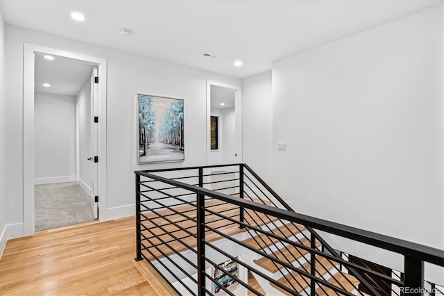 corridor featuring wood finished floors, baseboards, an upstairs landing, and recessed lighting
