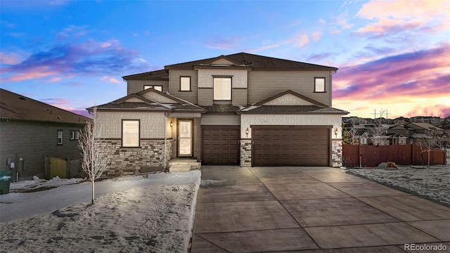 view of front of house with stone siding, driveway, an attached garage, and fence