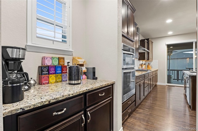 kitchen featuring stainless steel appliances, light stone countertops, dark brown cabinets, and dark wood-style flooring