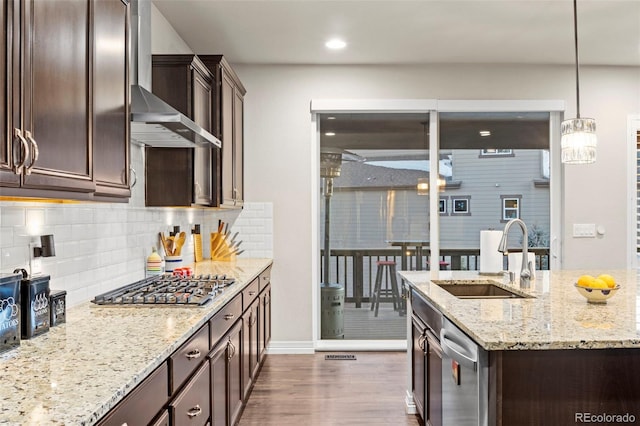 kitchen featuring dark brown cabinetry, stainless steel appliances, wall chimney range hood, and a sink