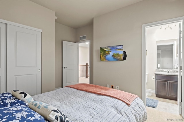 bedroom with ensuite bath, light colored carpet, and visible vents