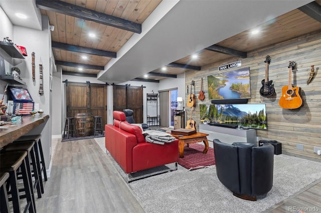 living room featuring beam ceiling, wood finished floors, a barn door, wooden ceiling, and wood walls