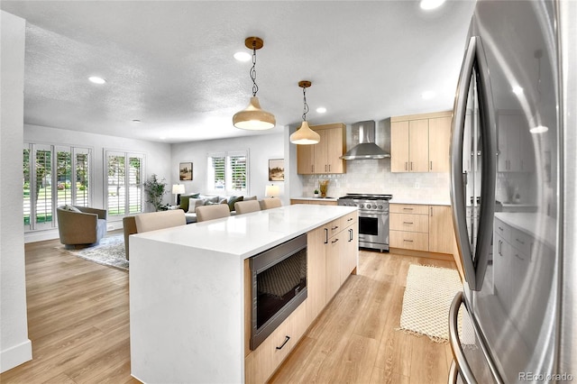 6716 W Rowland Ave, Littleton, CO 80128 - kitchen with stainless steel appliances, light brown cabinetry, wall chimney range hood, light countertops, and open floor plan