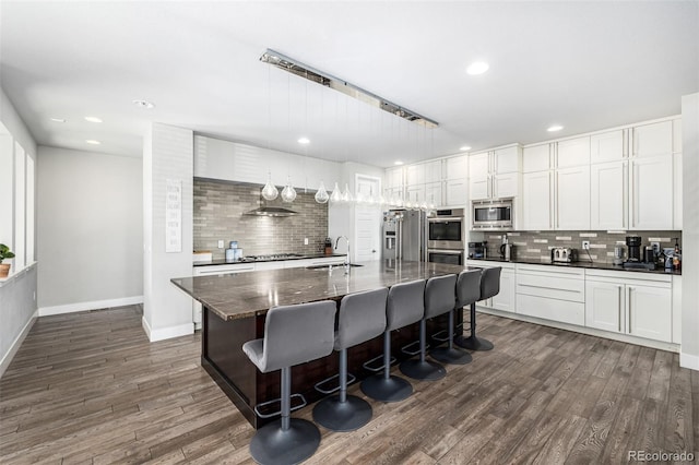 kitchen with pendant lighting, stainless steel appliances, dark hardwood / wood-style floors, and an island with sink