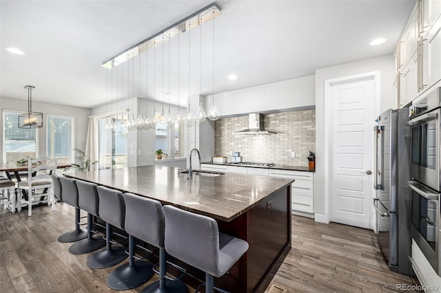 kitchen with dark wood-type flooring, white cabinets, sink, a kitchen island with sink, and pendant lighting