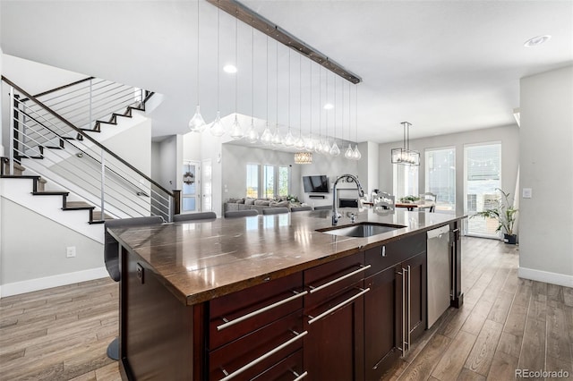 kitchen featuring pendant lighting, hardwood / wood-style floors, sink, an island with sink, and stainless steel dishwasher