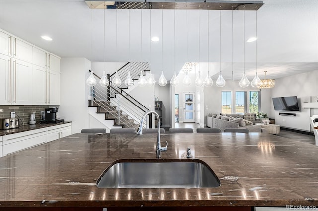 kitchen featuring white cabinetry, sink, backsplash, a chandelier, and pendant lighting