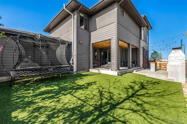 back of house featuring a trampoline, a patio, and a yard