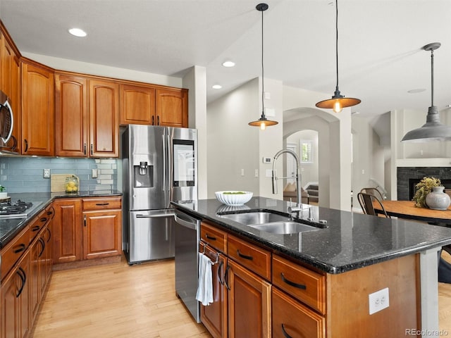 2821 Fulton St, Denver, CO 80238 - kitchen with appliances with stainless steel finishes, light wood-style flooring, arched walkways, dark stone countertops, and a center island with sink
