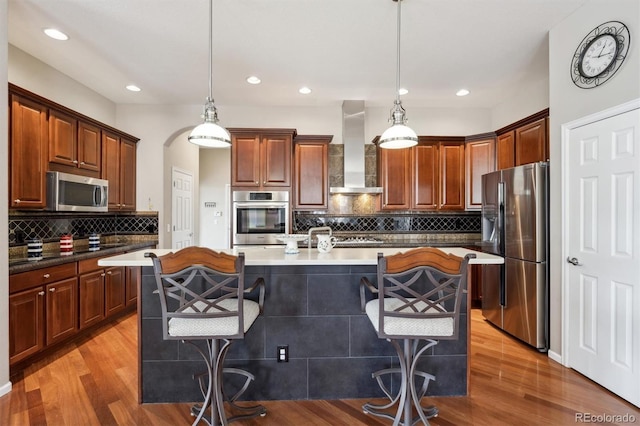 5810 Moss Ct, Golden, CO 80403 - kitchen featuring stainless steel appliances, wall chimney range hood, decorative backsplash, light wood-type flooring, and a breakfast bar area