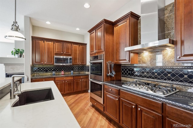 5810 Moss Ct, Golden, CO 80403 - kitchen featuring wall chimney range hood, appliances with stainless steel finishes, tasteful backsplash, light wood finished floors, and pendant lighting
