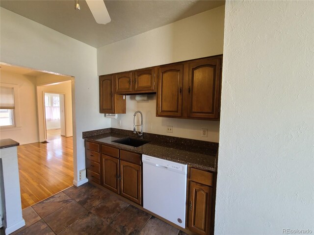 kitchen featuring white dishwasher, dark stone countertops, dark wood-type flooring, sink, and ceiling fan