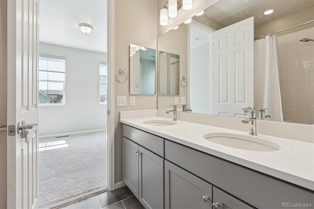 full bathroom with double vanity, a sink, baseboards, and a tile shower